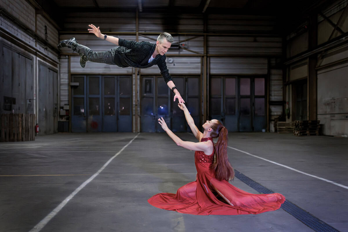 Impressive magic act with a magician flying above a woman in a red dress inside a warehouse.