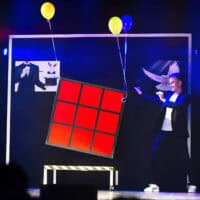 Magician & illusionist demonstrating a Rubik's Cube illusion on stage.